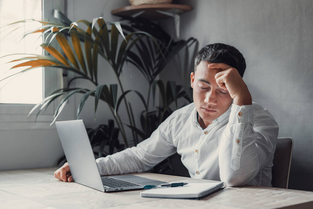 Εξαντλημένος και κουρασμένος άνθρωπος στο γραφείο με φορητό υπολογιστή. επιχειρηματίας με πονοκέφαλο και κλειστά μάτια  - Φωτογραφία, εικόνα
