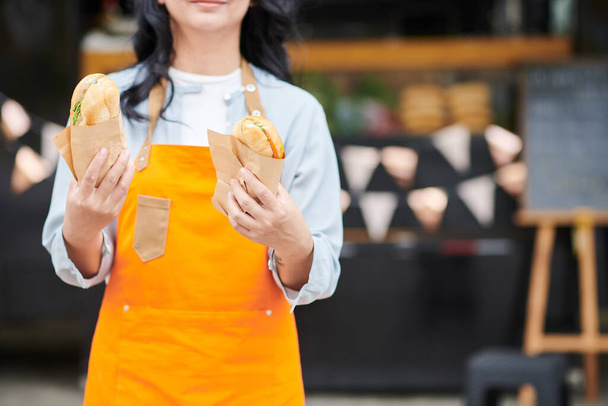 Oříznutý obrázek dělníka z jídelního vozu držícího dva sendviče se šunkou a čerstvými zeleninami - Fotografie, Obrázek