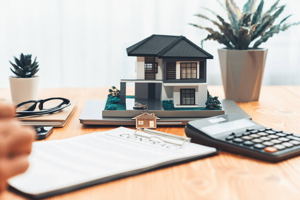 Model domu jest wyświetlany na drewnianym stole spotkań z w rozmytym tle agenta nieruchomości i klienta omówić warunki kredytu mieszkaniowego lub umowy najmu. Podmiot - Zdjęcie, obraz