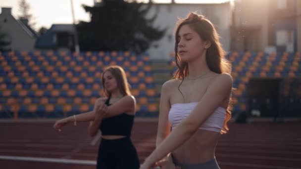 Twee meisjes slanke vrienden kwamen naar het stadion voor joggen of fitness, doen spieropwarming, ondersteunen elkaar, doen armoefeningen bij zonsondergang - Video