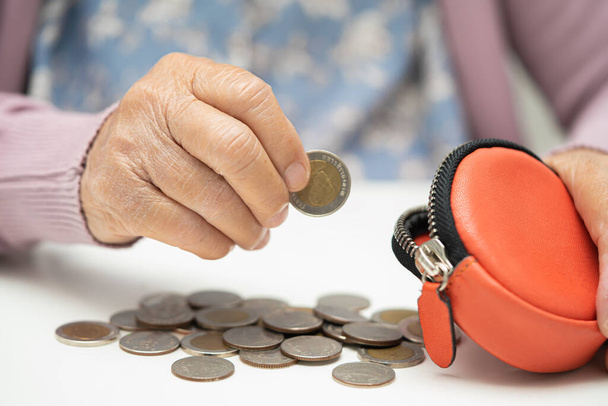 Mujer mayor asiática sosteniendo el conteo de moneda en el bolso. Pobreza, problema de ahorro en la jubilación. - Foto, imagen