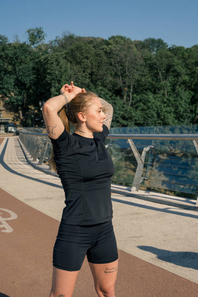 Fitness young sportswoman girl in morning doing warm-up exercises before training on the street in the city on the bridge Sport health - Photo, Image