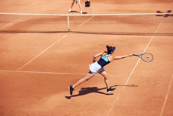 Top view image of young woman, tennis player in motion during game, swing ball at open air tennis court. Concentration. Concept of sport, hobby, active lifestyle, health, endurance and strength, ad - Zdjęcie, obraz