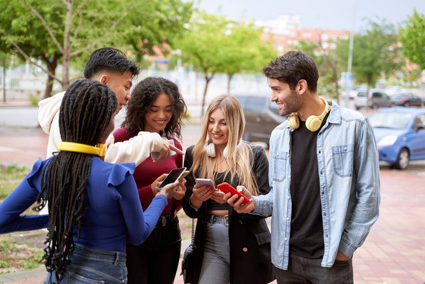 Ομάδα φίλων που κοιτάζουν τα κινητά τους ενώ στέκονται έξω μαζί. Έννοια φιλίας και τεχνολογίας. - Φωτογραφία, εικόνα