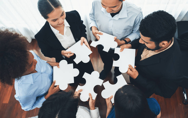 Diverse corporate officer workers collaborate in office, connecting puzzle pieces to represent partnership and teamwork. Unity and synergy in business concept by merging jigsaw puzzle. Concord - Photo, Image