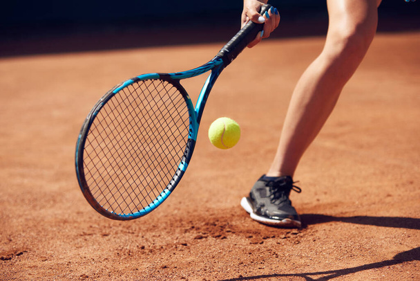 Cropped image of female legs in sportswear and tennis racket with ball over floor background with shadows. Open air tennis court. Concept of sport, hobby, active lifestyle, health, strength, ad - Zdjęcie, obraz