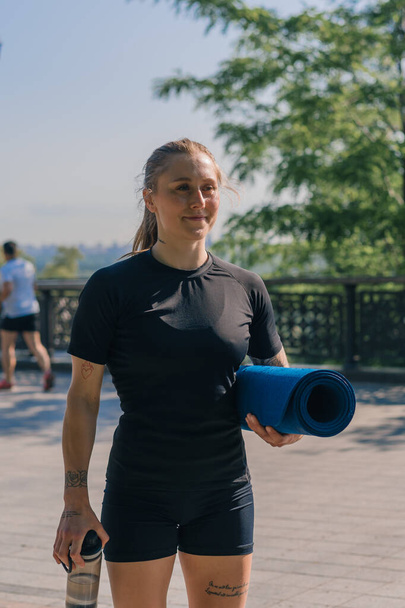 portret van een jonge glimlachende sportvrouw meisje met een kettlebell en een fles water in haar handen voordat ze een training buiten in het park begint - Foto, afbeelding