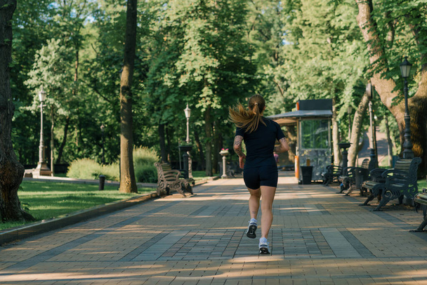 Γυμναστική νεαρή αθλήτρια κορίτσι κάνει σπορ το πρωί τρέχει κατά τη διάρκεια της κατάρτισης σε εξωτερικούς χώρους στην πόλη στο πάρκο έννοια του υγιεινού τρόπου ζωής - Φωτογραφία, εικόνα