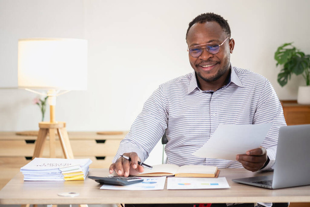 Hombre de negocios afroamericano sonriendo relajado y cruzó los brazos después de análisis e investigación en la oficina del hogar - Foto, Imagen