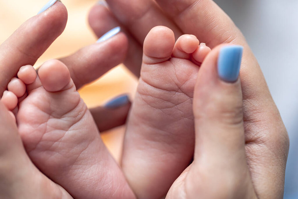 Anya tartja a lábát egy újszülött baba a kezében, közelkép, lágy fókusz, koncepció az anyaság és a gondozás. - Fotó, kép