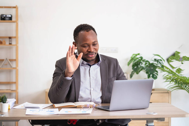 Afro-Amerikaanse zakenman analyseren laptop grafiek papierwerk in kantoor met documenten voor de voorbereiding van portfolio-analyse rapport Zwarte mannelijke analist doet papierwerk op de werkplek met behulp van de computer. - Foto, afbeelding