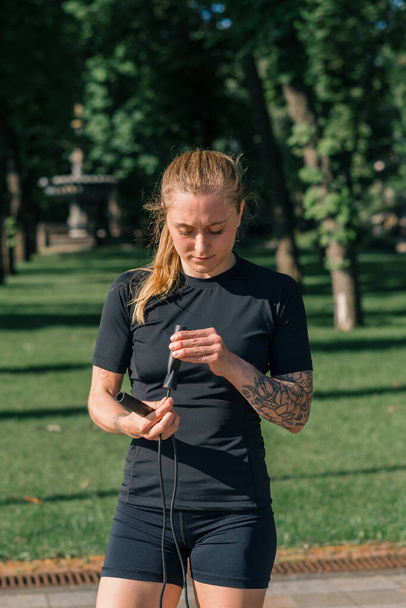 Fitness jonge sportvrouw meisje met tatoeages in de ochtend doet sport ontwarren touw tijdens het sporten buiten in de stad in park Sport gezondheid - Foto, afbeelding