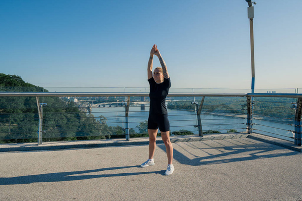 Fitness nuori urheilija tyttö aamulla tekee lämpeneminen harjoituksia ennen koulutusta kadulla kaupungin sillalla Urheilu terveys - Valokuva, kuva