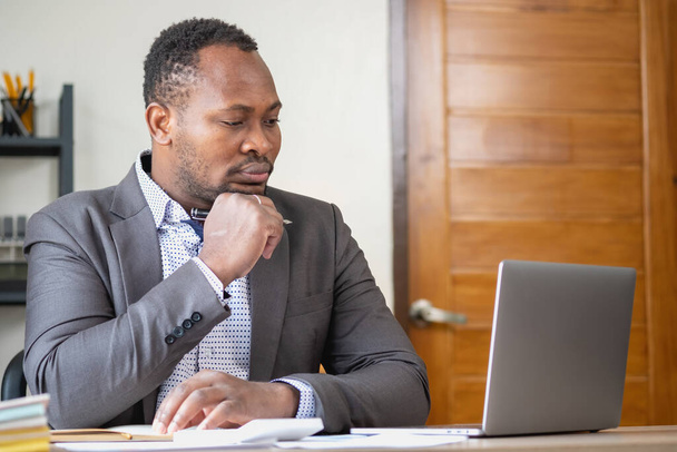 Un homme d'affaires afro-américain en costume noir souriant et montrant de la joie au profit annuel de l'entreprise pour renforcer la confiance des clients qui investiront dans le bureau. - Photo, image