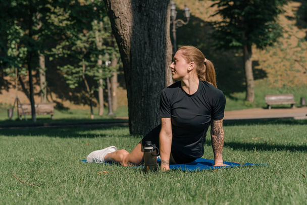 молодая спортсменка, занимающаяся физическими упражнениями на спортивной коврике для йоги на открытом воздухе в парке на траве концепции здорового образа жизни - Фото, изображение