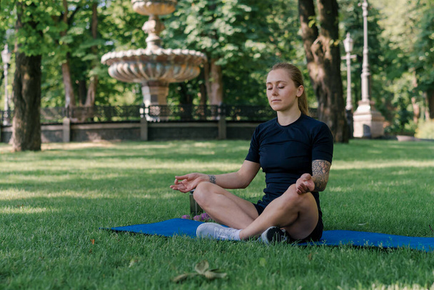 portret van jong sportief meisje mediteren doen yoga op sport mat buiten tijdens het sporten park gezonde levensstijl concept - Foto, afbeelding