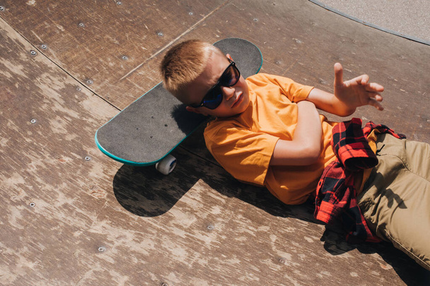 Atividades ao ar livre para crianças. Um menino alegre em óculos de sol está em um skate no playground. Um estudante caucasiano a passear. Vista superior - Foto, Imagem