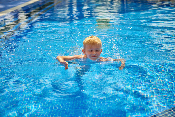 Niño pequeño niño de ocho años chapoteando en la piscina teniendo diversión actividad de ocio. Niño feliz nadando en una piscina. Actividades en la piscina, niños nadando y jugando en el agua, la felicidad y - Foto, Imagen