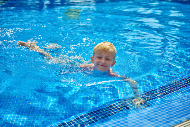 Young boy kid child eight years old splashing in swimming pool having fun leisure activity. Boy happy swimming in a pool. Activities on the pool, children swimming and playing in water, happiness and - Foto, Imagen