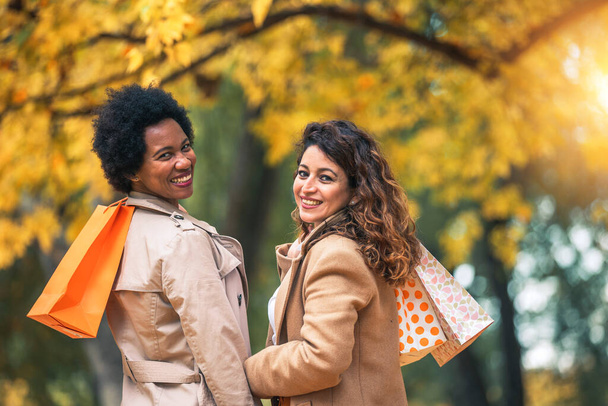 Glückliche Freundinnen spazieren im Herbst mit Einkaufstüten durch den Wald. - Foto, Bild
