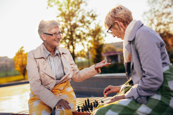 Dos mujeres mayores jugando ajedrez y divirtiéndose con él en el colorido parque en el otoño - Foto, imagen