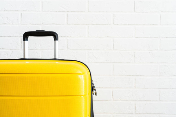 Желтый багаж чемодан возле стены белого кирпича в студии. - Фото, изображение