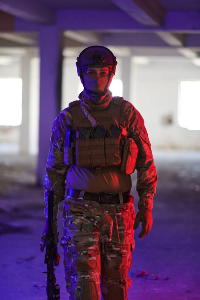 A professional soldier undertakes a perilous mission in an abandoned building illuminated by neon blue and purple lights.  - Foto, Imagen