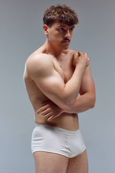 Handsome young man with muscular body posing shirtless in underwear against grey studio background. Relief hands. Concept of mans beauty, sport, health, athletic body, medicine - 写真・画像