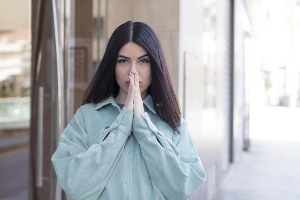 young pretty woman feeling worried, hopeful and religious, praying faithfully with palms pressed, begging forgiveness - Valokuva, kuva