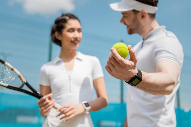 focus on ball, blurred man looking at girlfriend, teaching how to play tennis on court, sport - Photo, Image