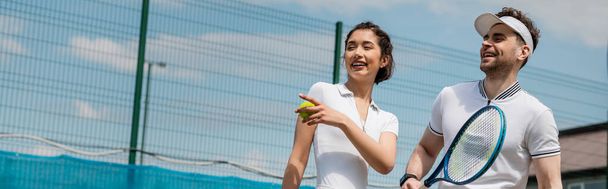 πανό, χαρούμενη γυναίκα που δείχνει μακριά, άντρας που χαμογελάει και κρατάει ρακέτα του τένις, καλοκαίρι, ζευγάρι αθλήματα - Φωτογραφία, εικόνα