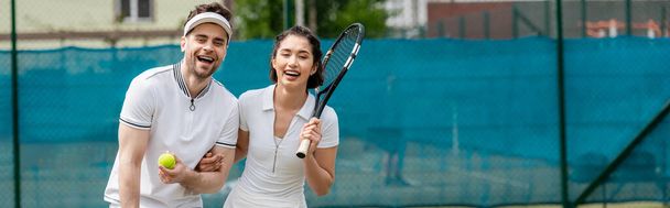banner, cheerful couple in active wear holding rackets and ball near tennis net, hobby and sport - Photo, Image