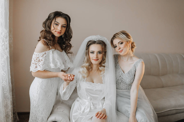 The bridesmaids are looking at the camera. The bride and her fun friends celebrate the bachelorette party in different dresses. Bride and friends in the room - Zdjęcie, obraz