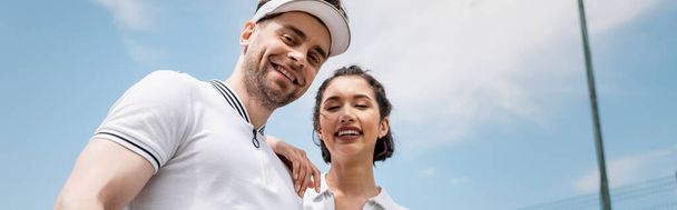 banner, cheerful couple in active wear looking at camera on tennis court, hobby and sport - Photo, Image