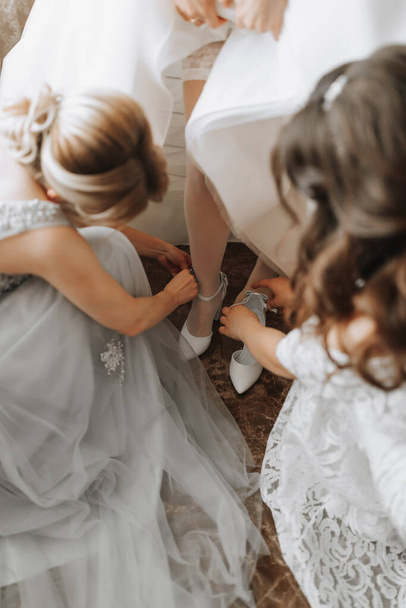 Girlfriends help the bride put on her wedding shoes. Beautiful female legs close-up - Valokuva, kuva