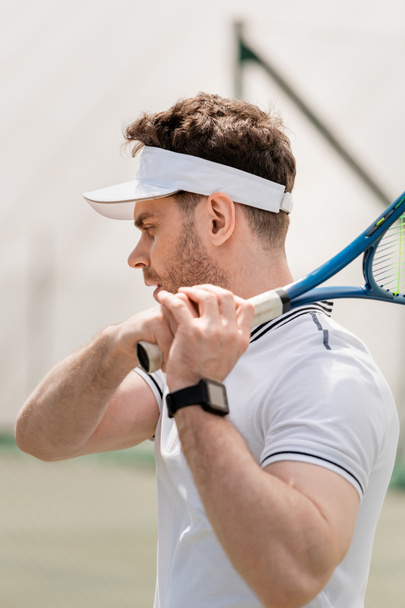 handsome tennis player in sports visor holding racket on court, motivation and sport - Foto, imagen