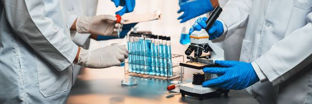 Grupa dedykowanych naukowców przeprowadza eksperyment chemiczny przy użyciu mikroskopu w laboratorium medycznym w celu opracowania nowego leku szczepionkowego lub antybiotyku. Laboratorium biotechnologiczne i koncepcja badań medycznych. Neoterynowy - Zdjęcie, obraz