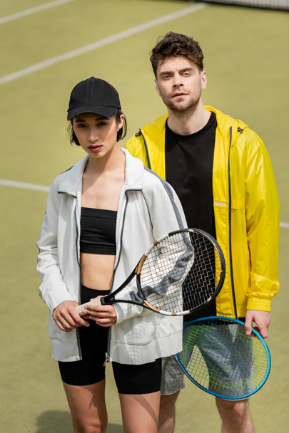 deporte y estilo, hombre y mujer de moda en ropa deportiva con raquetas de tenis en la cancha - Foto, Imagen