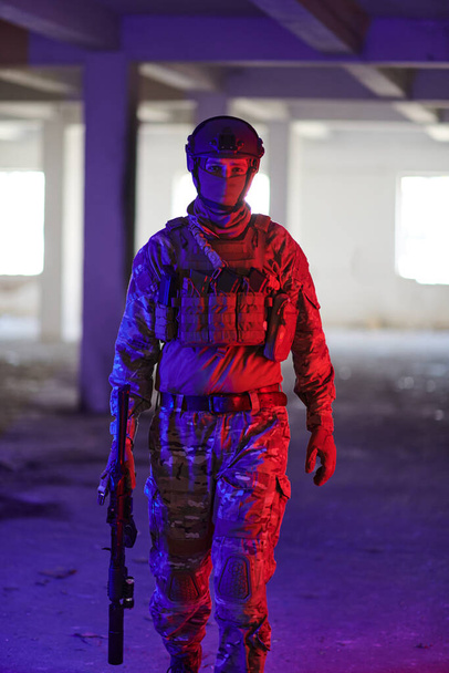 A professional soldier undertakes a perilous mission in an abandoned building illuminated by neon blue and purple lights.  - Фото, зображення