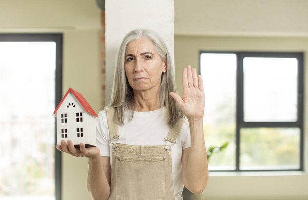 pretty senior woman looking serious showing open palm making stop gesture. with a house model - Fotoğraf, Görsel