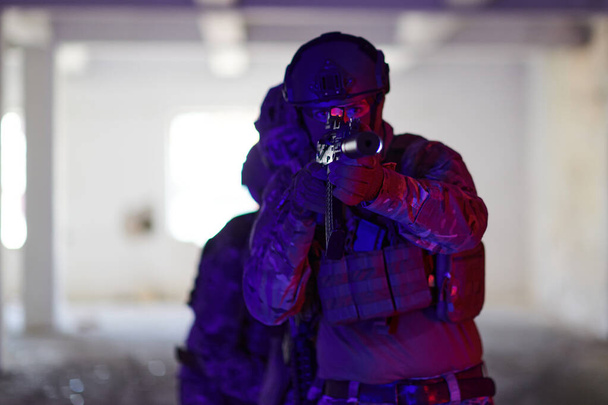 A professional soldier undertakes a perilous mission in an abandoned building illuminated by neon blue and purple lights.  - 写真・画像