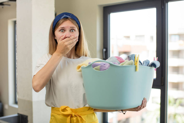 young pretty woman covering mouth with a hand and shocked or surprised expression. laundry and wash clothes concept - Photo, image
