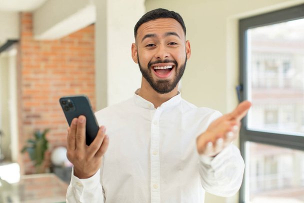 young  adult man smiling happily and offering or showing a concept. smartphone concept - Foto, afbeelding