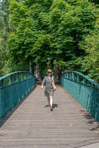 Straatsburg straat: Een vrouw met een strohoed met een blauw lint loopt over een brug van de stad - Foto, afbeelding