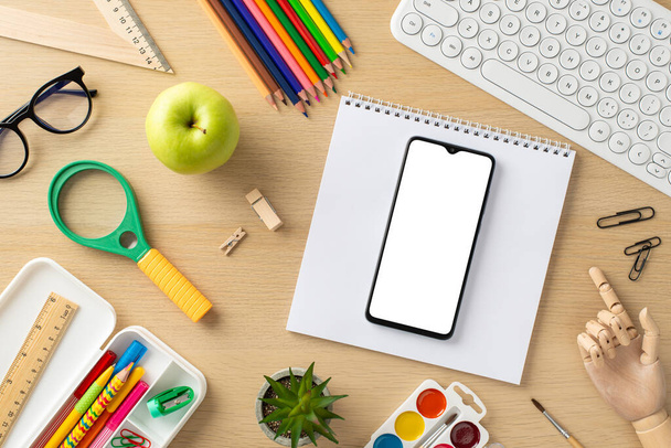 Immerse yourself in the digital learning era with this top-view composition, featuring a keyboard, smartphone, notebook, pencil case with stationery and glasses on wooden background - Foto, Imagen