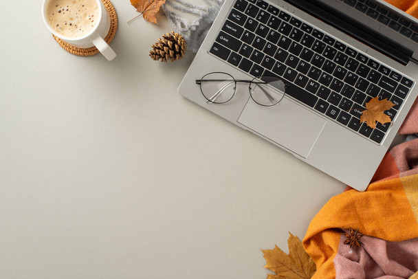 Top view image encapsulates the essence of working from home, showcasing a laptop with a cozy blanket, pinecones, spices, glasses and a cup of coffee on grey isolated backdrop with copyspace for text - Фото, изображение