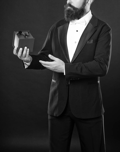 copped man in tuxedo bow tie formalwear on black background presenting box. shopping sale. - Foto, Imagem