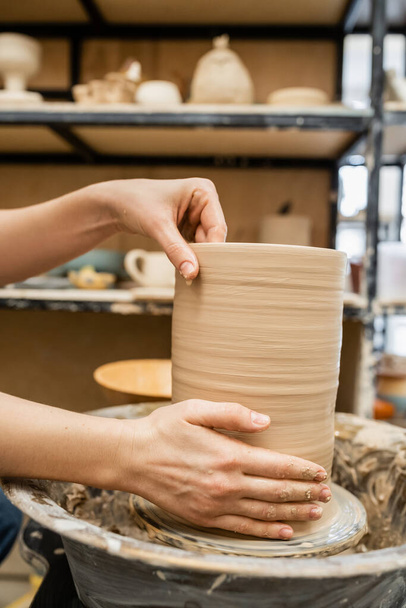 Vista recortada de las manos de la artesana haciendo jarrón de arcilla en la rueda de cerámica en el taller - Foto, Imagen