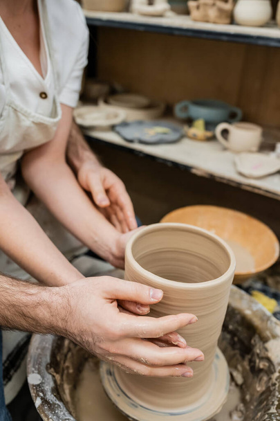 Cropped view of couple in love making clay vase together on pottery wheel in ceramic workshop - Foto, imagen