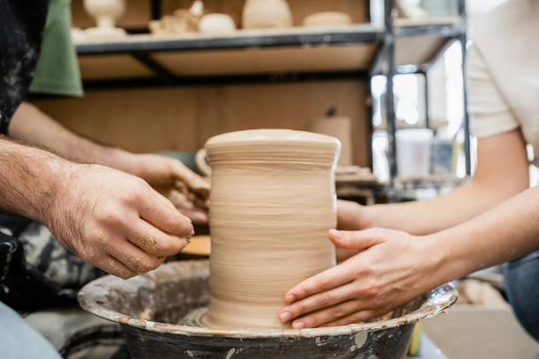 Vista recortada de románticos artesanos moldeando jarrón de arcilla sobre rueda de cerámica juntos en estudio de cerámica - Foto, imagen
